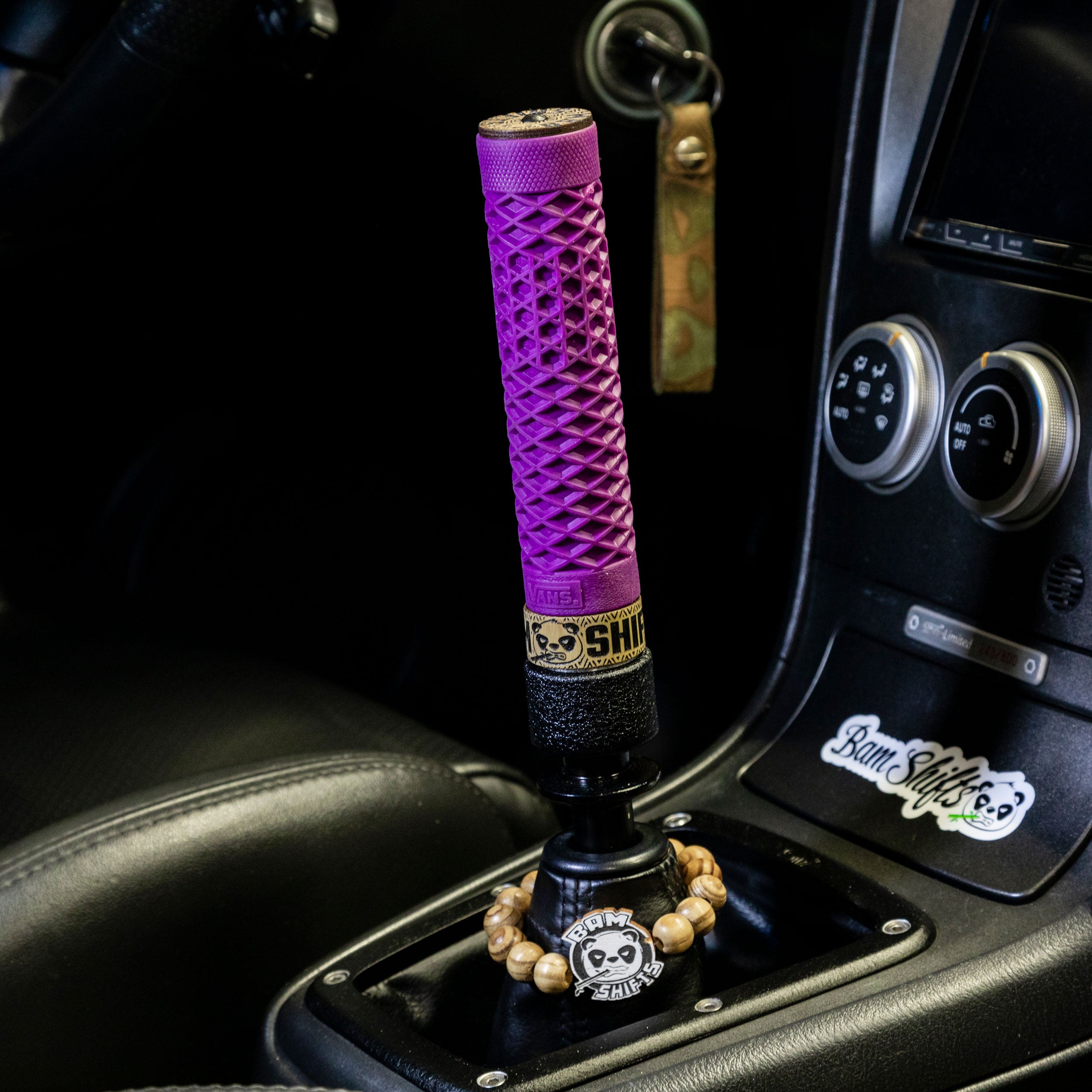 Purple gear shift knob with 'Bam Shifts' branding in a car console.