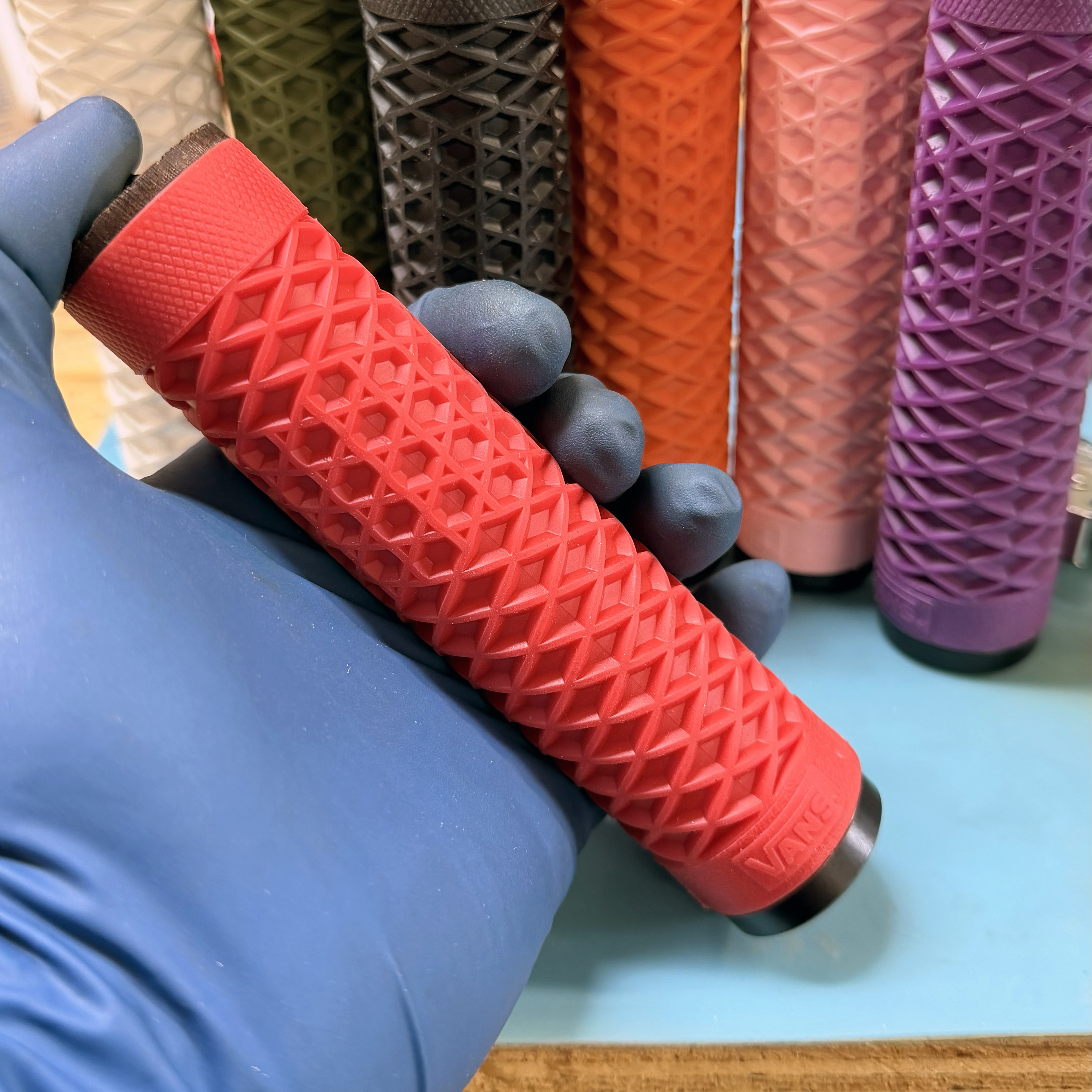 Red textured roller handle held by a gloved hand with colorful rollers in the background.